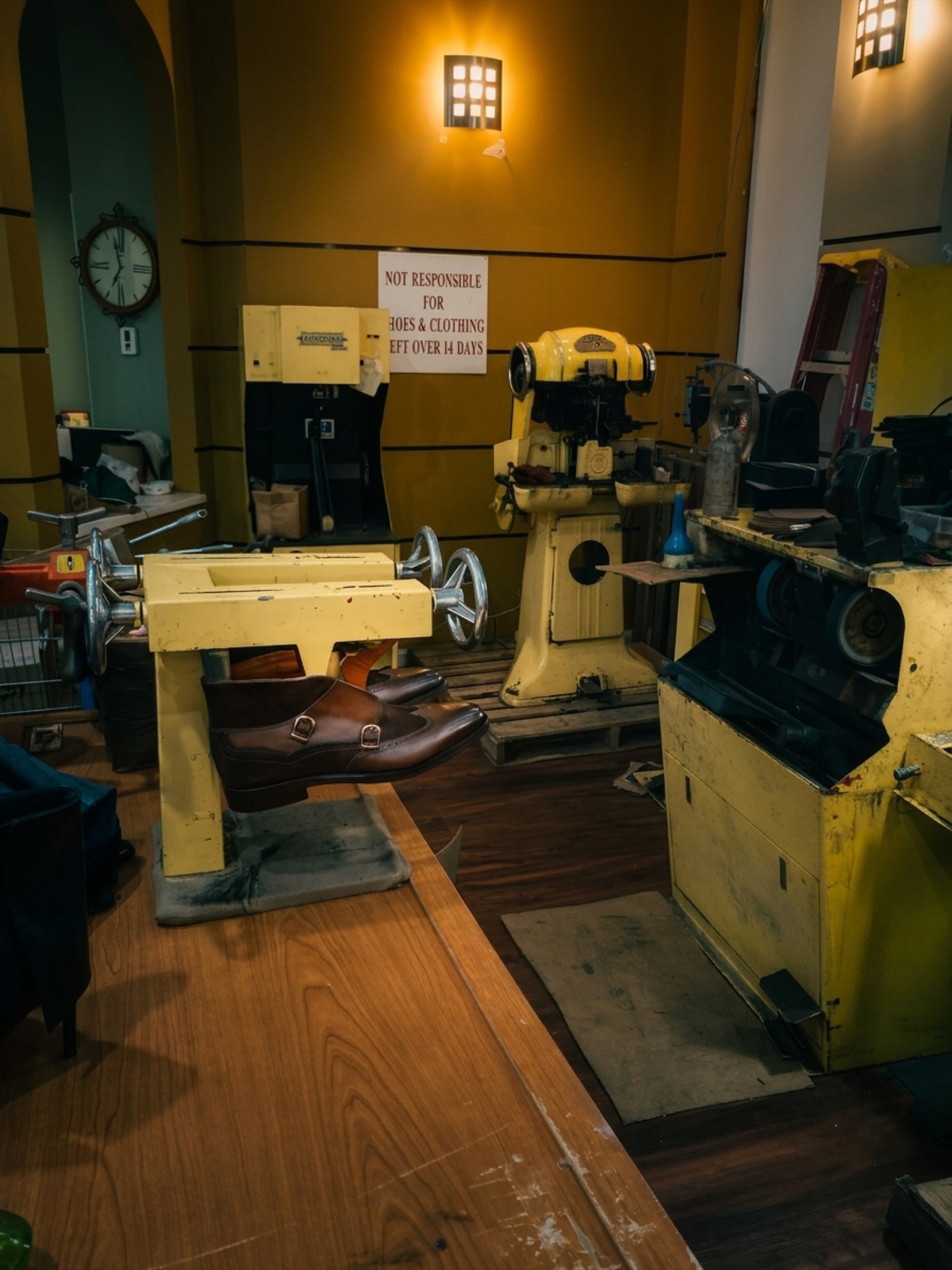 A pair of brown leather monk-strap shoes mounted on the yellow stretching machine under warm sconce light.